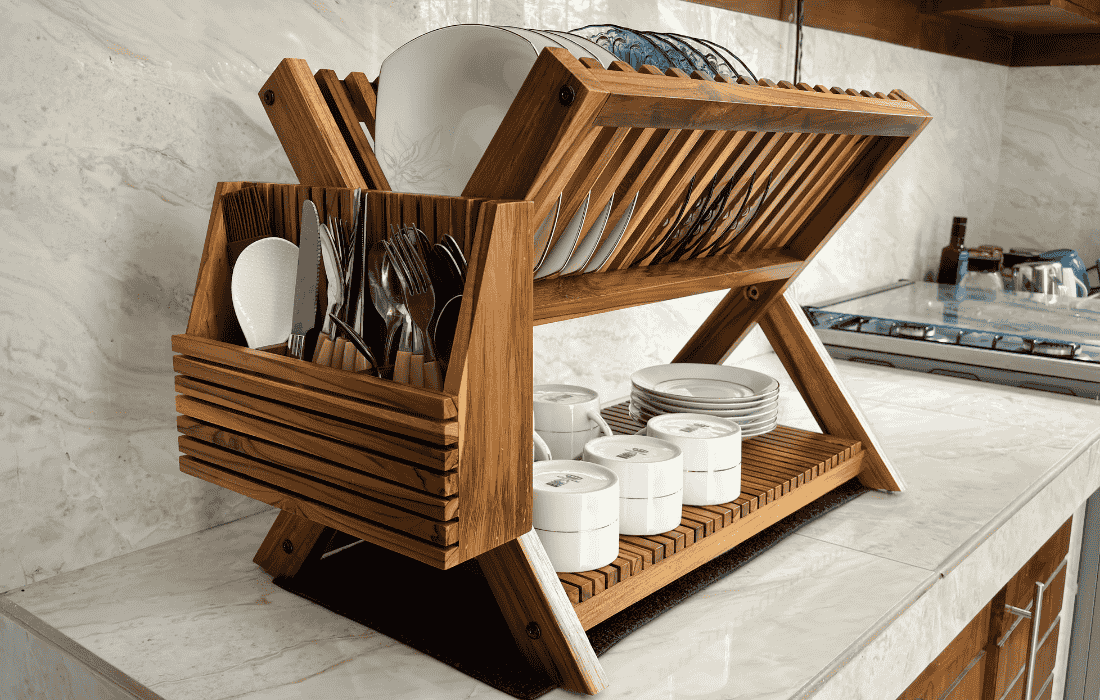 Handmade teak wood dish drying rack with plates, utensils, and bowls organized on kitchen countertop