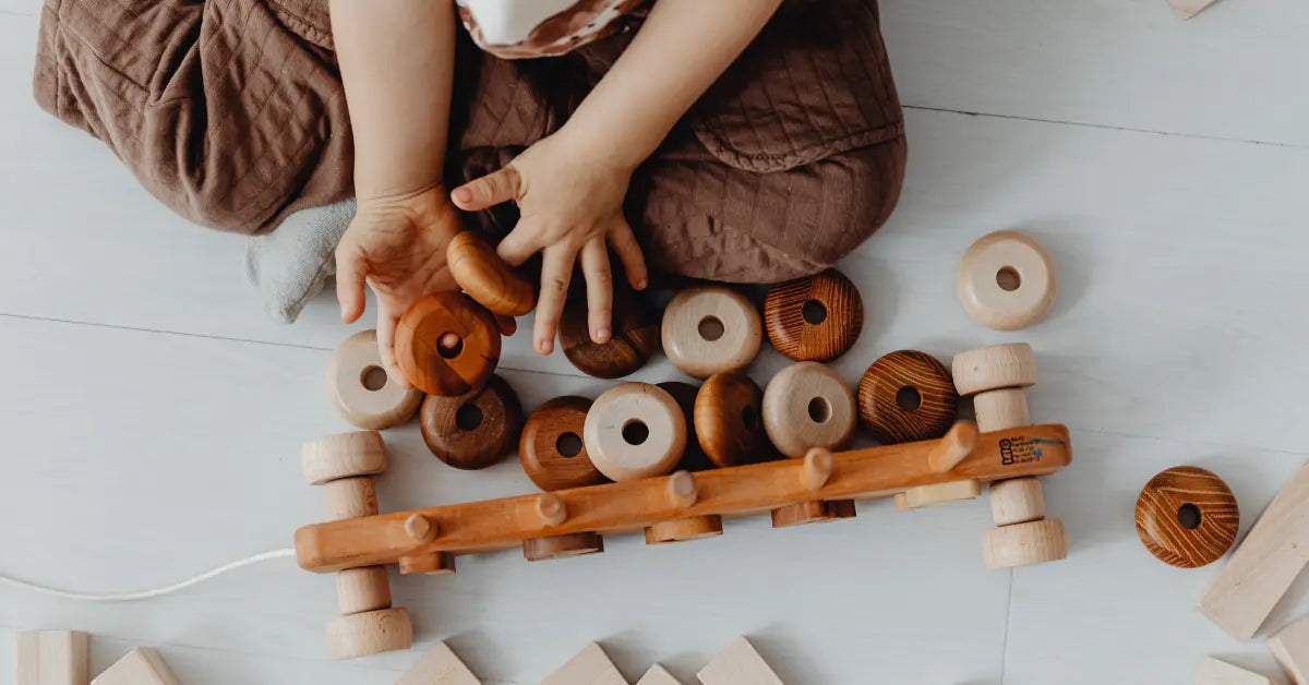 Child playing with eco-friendly wooden toy cars and wooden blocks on a light floor