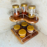 Wood Ceylon corner spice rack with two-tier wooden shelves and metal railing holding jars with gold lids