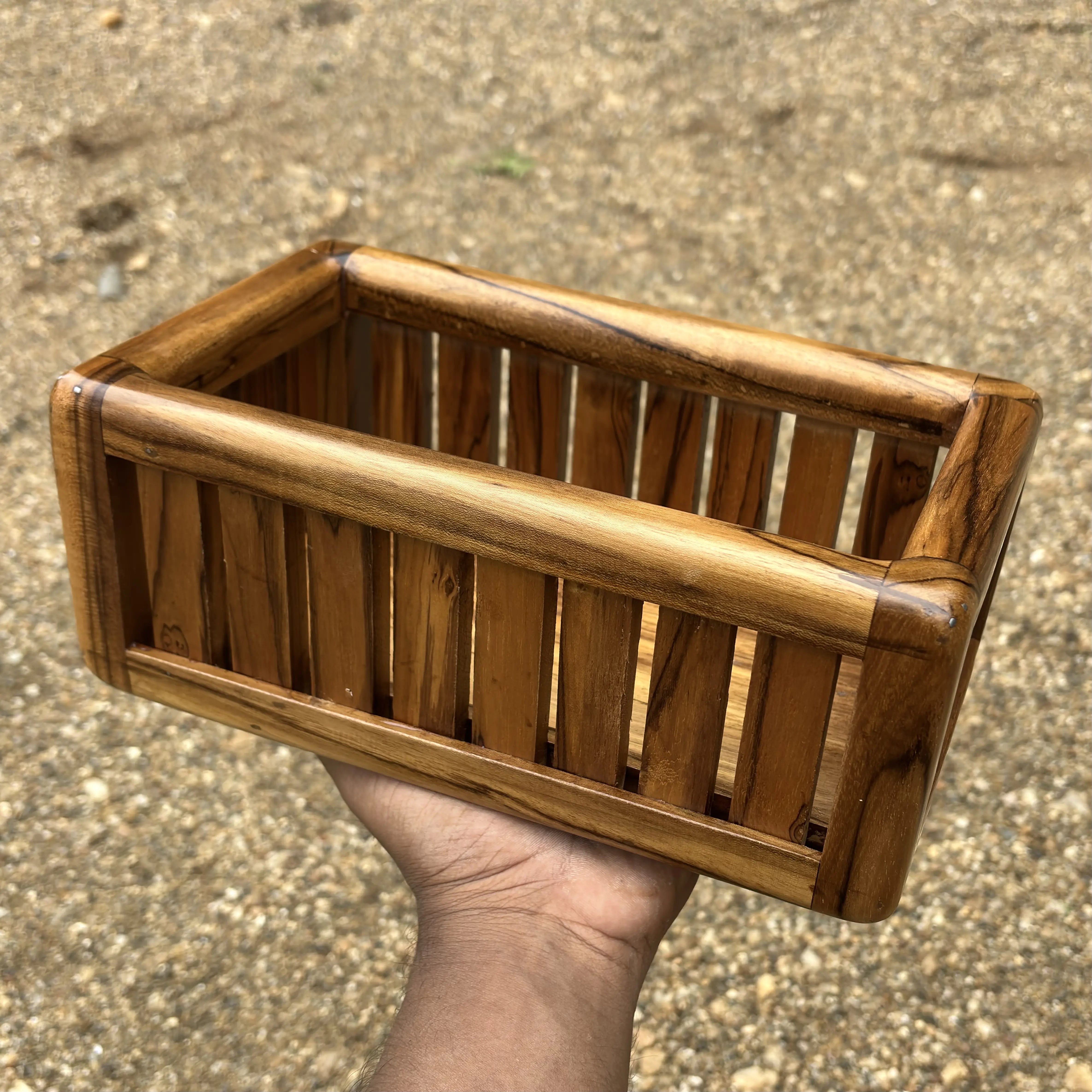 Wooden towel box storage handcrafted by Wood Ceylon held in a hand on a gravel background