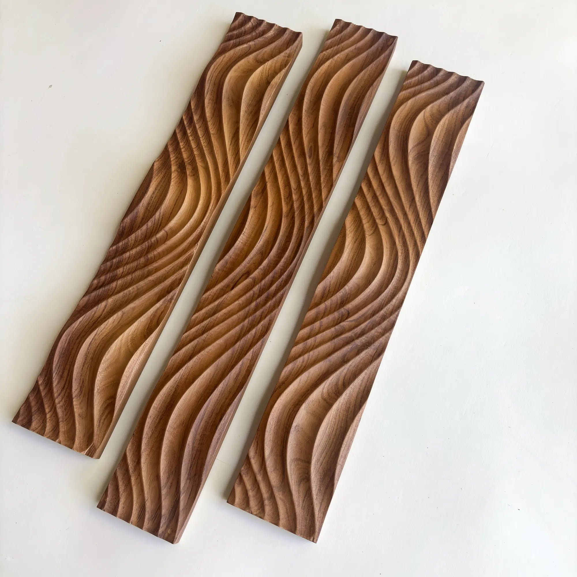 Three intricately carved solid teak wood panels showing elegant wave patterns
