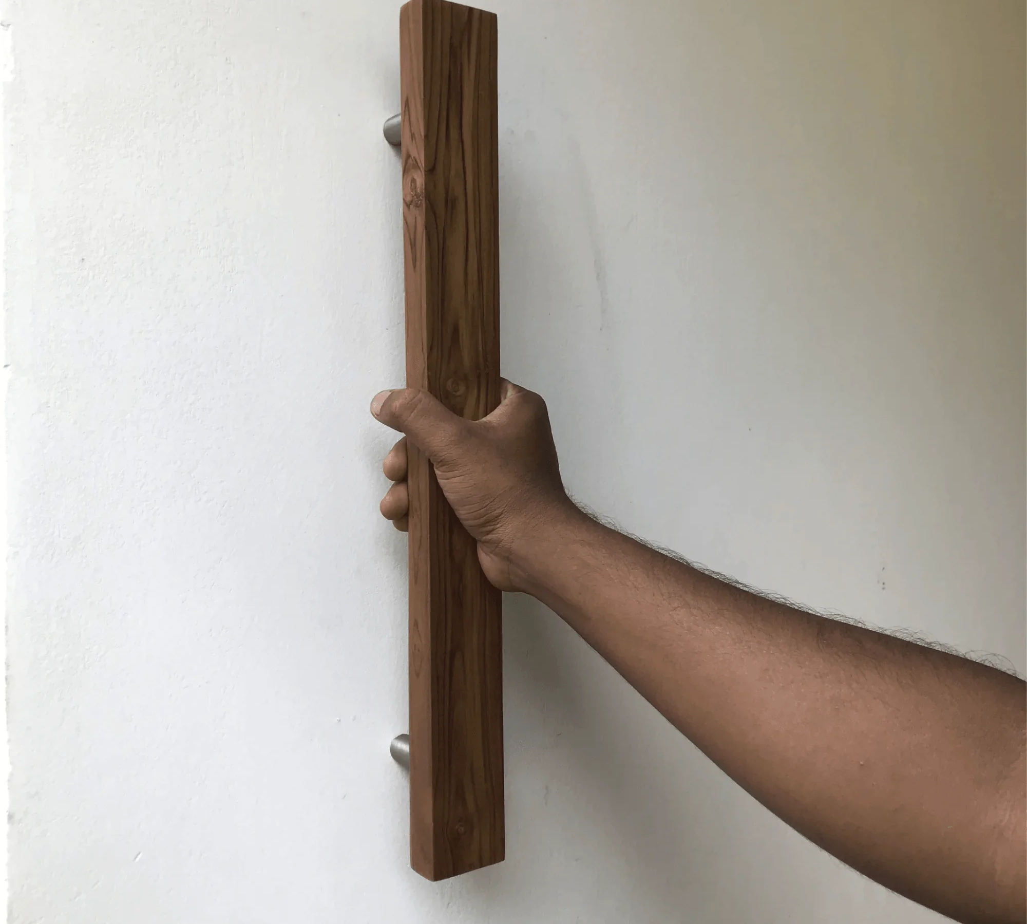 Hand holding a sleek teak barn door handle with a modern design for stylish home entryways