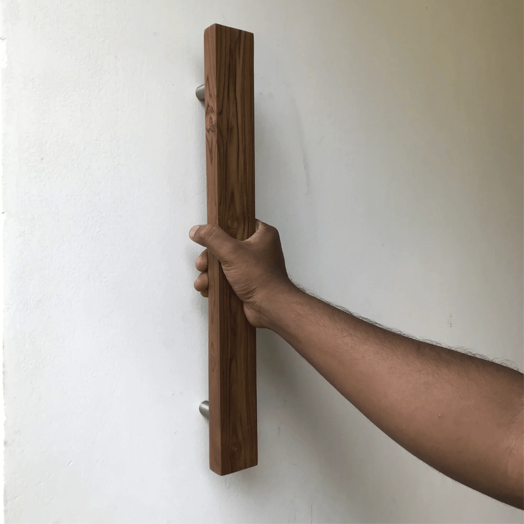 Hand holding a sleek teak barn door handle with a modern design for stylish home entryways