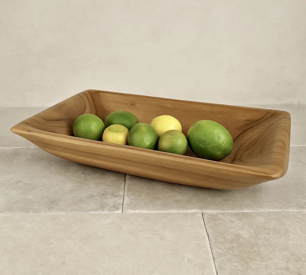 Elegant teak wood serving bowl filled with fresh limes and lemons on a stone countertop