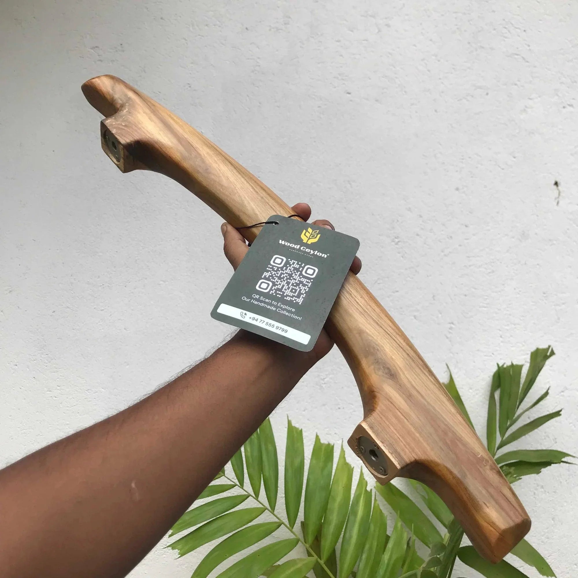 Hand holding a Wood Ceylon handmade teak door handle with natural wood grain and product tag