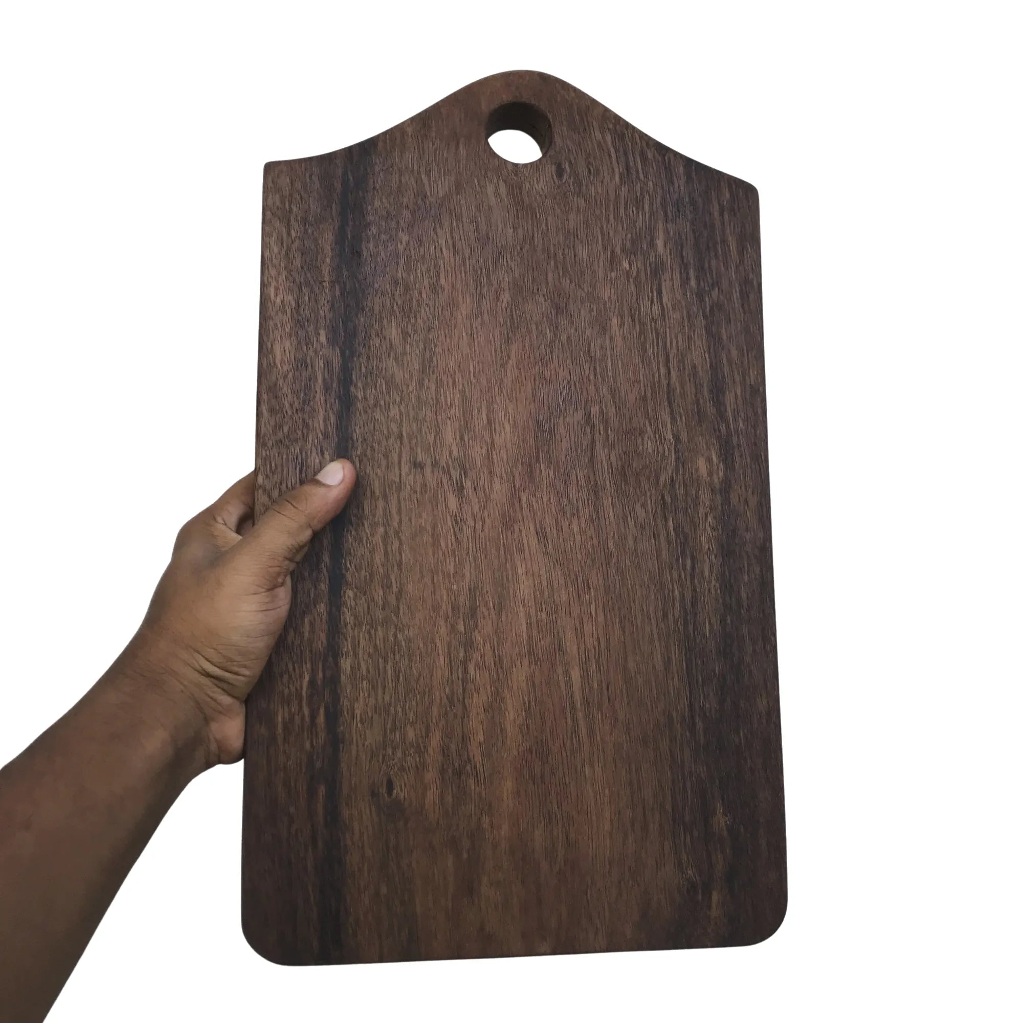 Hand holding a dark brown wood cutting board with a hole near the top for hanging