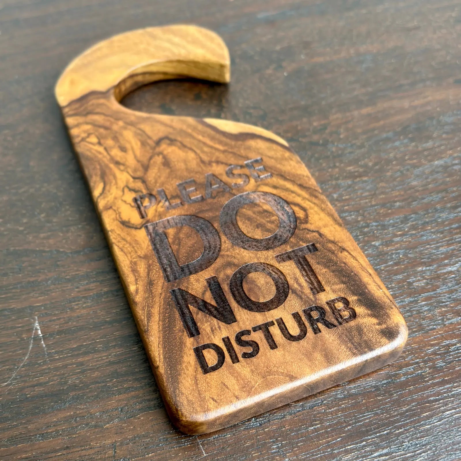 Wooden door sign hanger with Please Do Not Disturb text by Wood Ceylon on dark wood surface