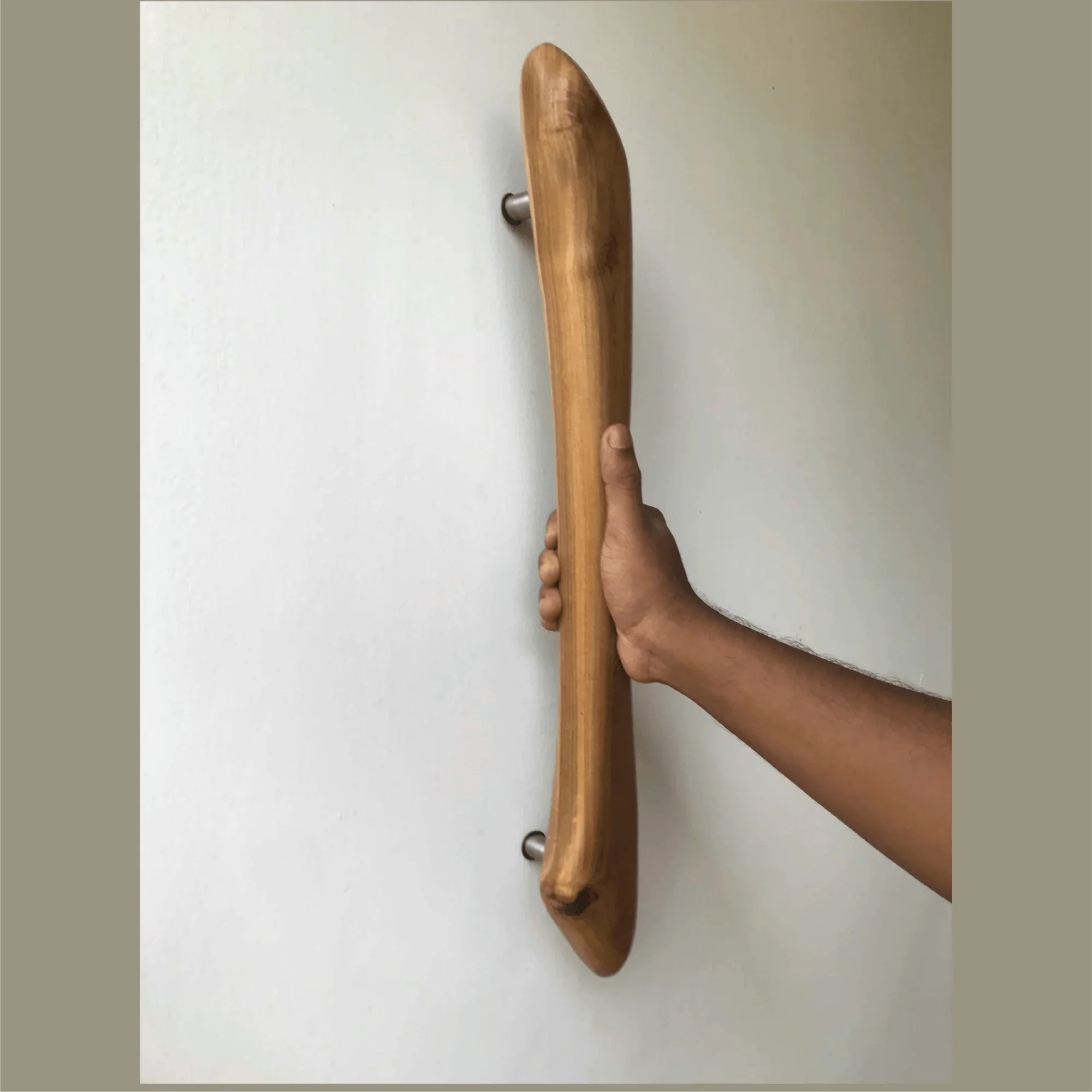 Hand gripping smooth curved wooden front door handle mounted on white wall by Wood Ceylon