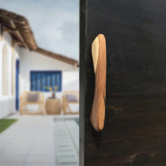 Wood Ceylon wooden front door handle hardware mounted on a dark door with a blurred outdoor background