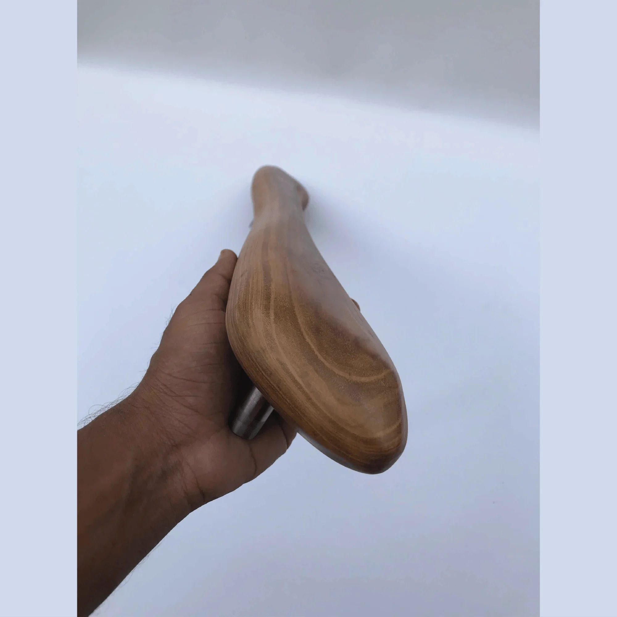 Hand holding a smooth polished wooden front door handle with natural wood grain finish