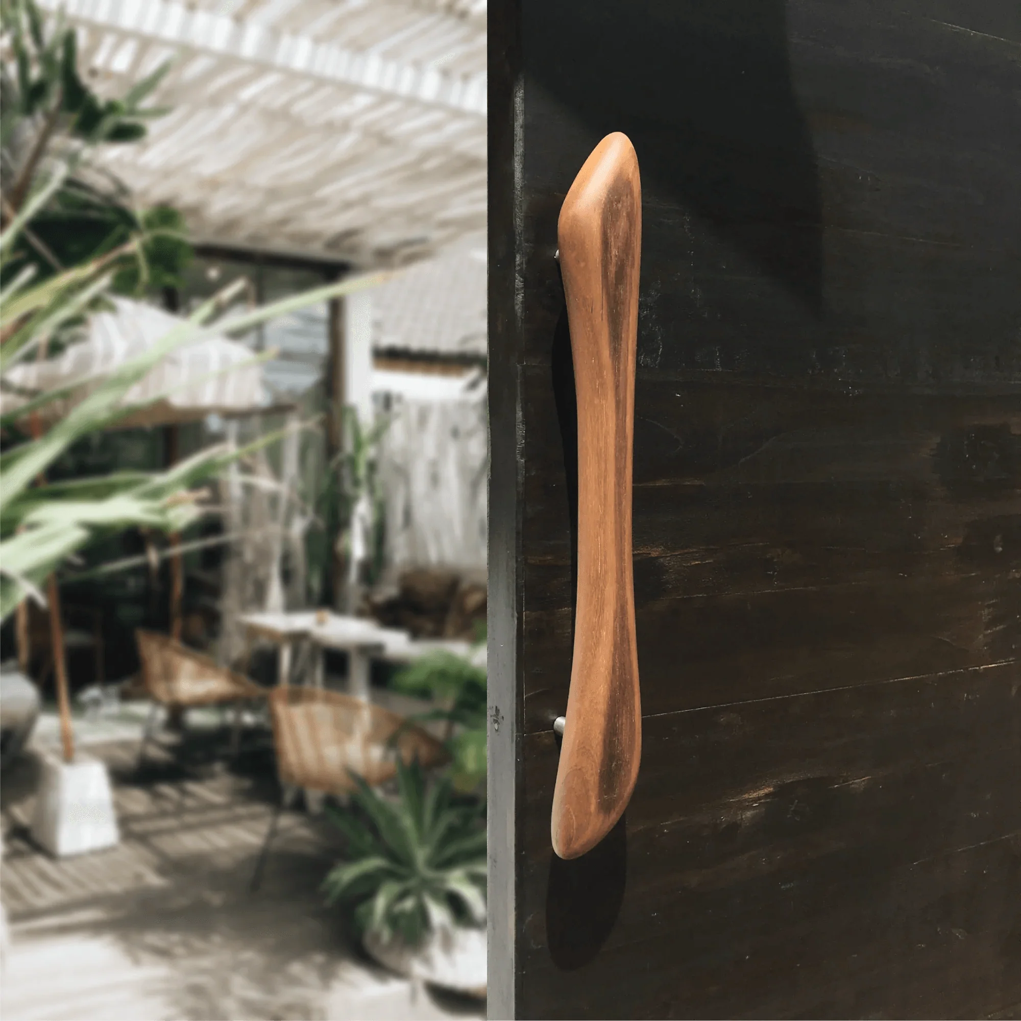 Wooden front door handle by Wood Ceylon mounted on a dark wooden door in a modern outdoor setting