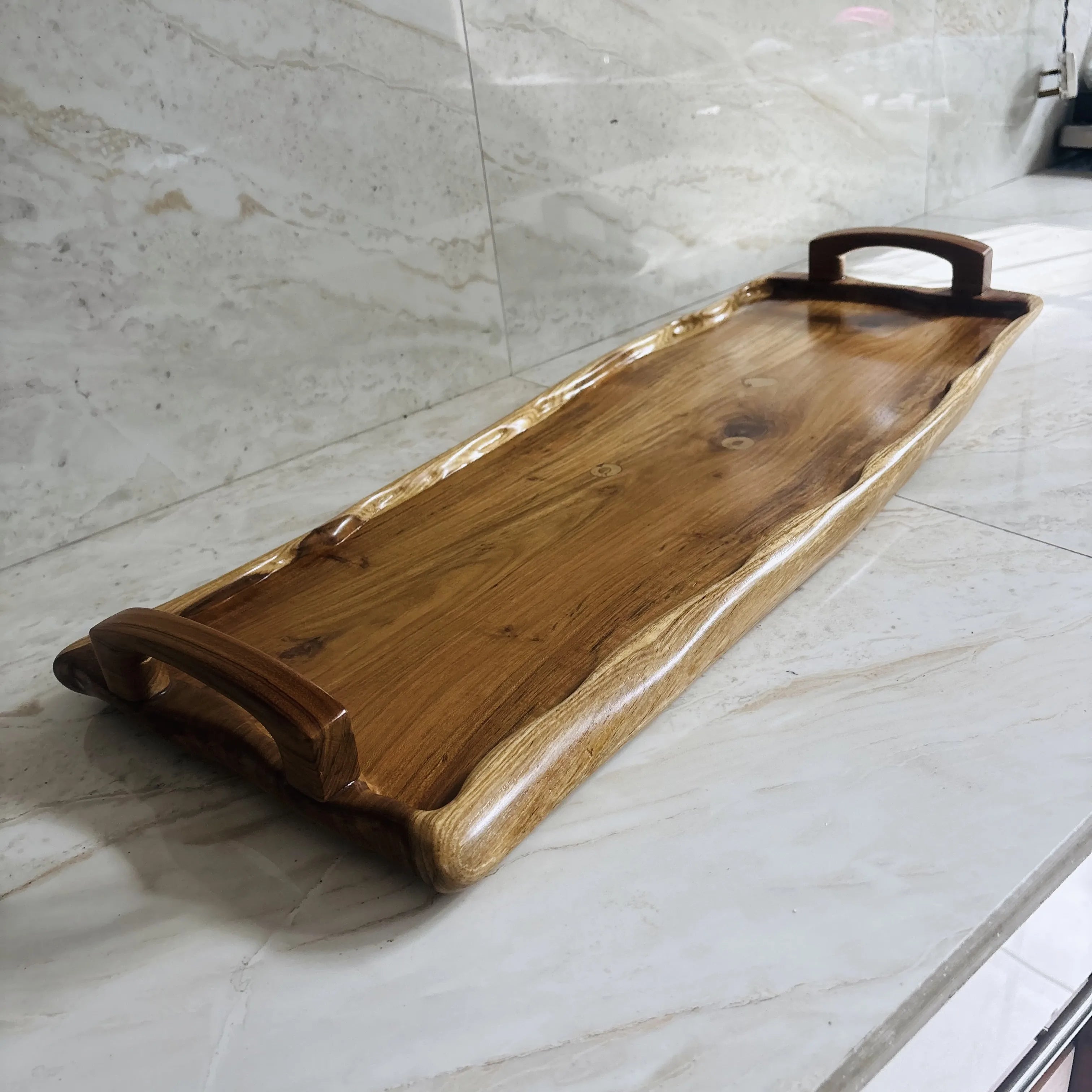 Wood Ceylon long wooden serving tray with handles and natural wood finish on marble surface